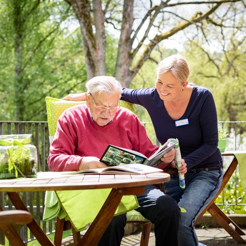Frau Böhm liest gemeinsam mit einem Bewohner auf dem Balkon ein Buch.