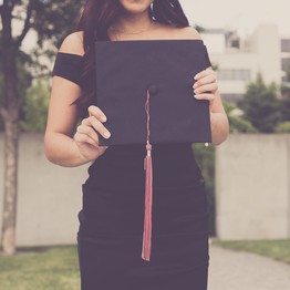 Eine junge Frau hält auf ihrer Abschlussfeier der Universität ihren Absolventenhut in die Kamera