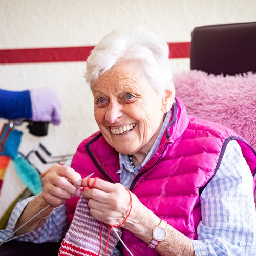 Eine lächelnde Bewohnerin beim Stricken, die nebenbei ein Gespräch mit der Beschäftigungstherapeutin führt.